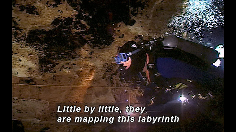 Person in scuba gear swimming in a cave. Caption: Little by little, they are mapping this labyrinth