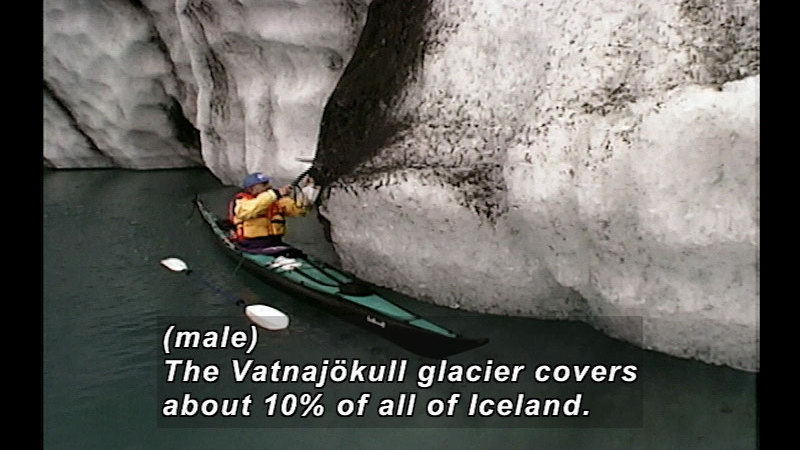 Person in a kayak next to glaciers reaching up towards the sheet of ice. Caption: (male) The Vatnajökull glacier covers about 10% of all of Iceland.