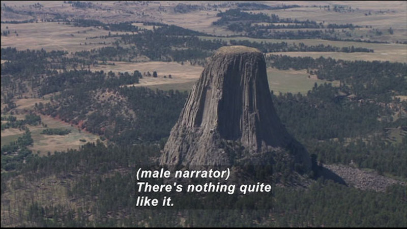 Rock formation rises sharply from evergreen tree covered ground to end in a narrowed flat-topped peak. Caption: (male narrator) There's nothing quite like it.