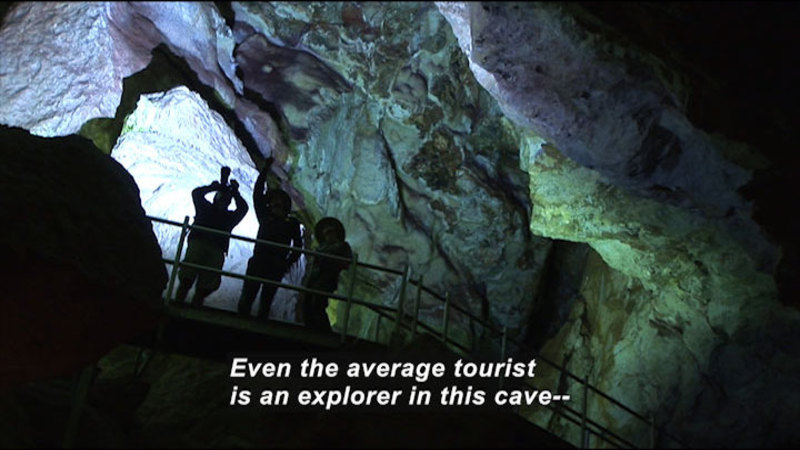 People standing on an overlook in a cave. Caption: Even the average tourist is an explorer in this cave--