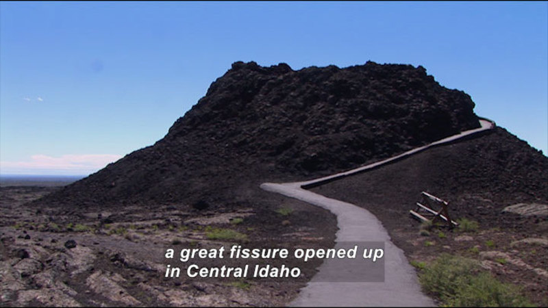 Narrow paved path spiraling to the top of a rocky conical structure. Caption: a great fissure opened up in Central Idaho
