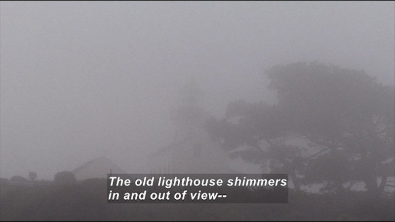 Lighthouse with outbuilding and trees as seen through dense fog. Caption: The old lighthouse shimmers in and out of view--