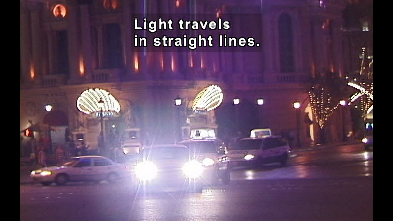 Straight on view of a car's headlights. Caption: Light travels in straight lines.