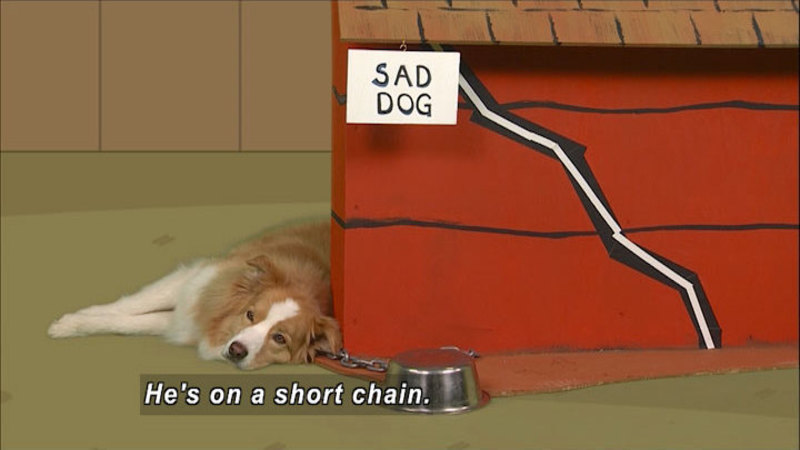 Dog laying at the front of a doghouse with a sign attached with Caption: sad dog. Food bowl is upside down by his head, chain attached to the ground and the dog. Caption: He's on a short chain.