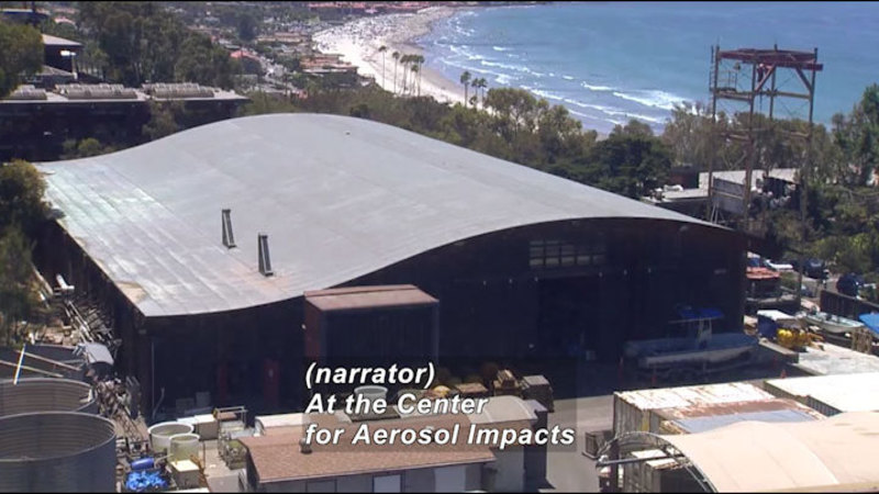 A large warehouse with a sloping roof. Caption: (narrator) At the Center for Aerosol Impacts