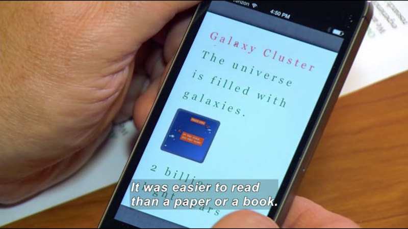 Person holding a smartphone displaying "Galaxy Cluster - The universe is filled with galaxies. 2 billion light years". Caption: It was easier to read than a paper or a book.