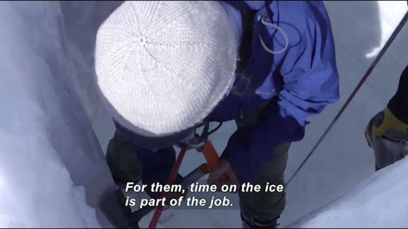 Person working on a large vertical sheet of ice. Caption: For them, time on the ice is part of the job.