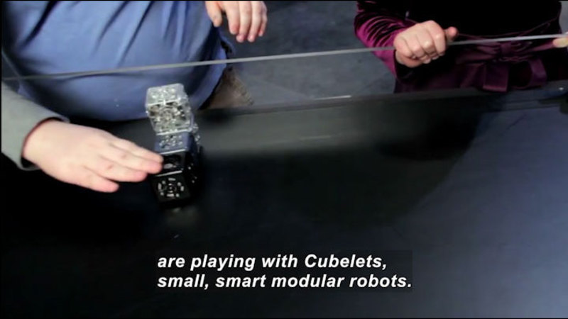 Person touching an object made of stacked and connected cubes. Caption: are playing with Cubelets, small, smart modular robots.
