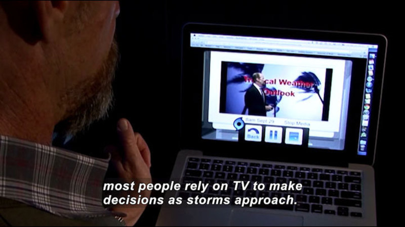 Person watching a newscast on a laptop. Caption: most people rely on TV to make decisions as storms approach.