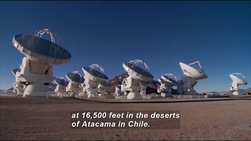 A cluster of telescopes pointed to the sky. Caption: at 16,500 feet in the deserts of Atacama in Chile.