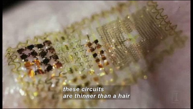 Closeup view of very thin wires forming concentric squares and other geometric patterns. Caption: these circuits are thinner than a hair