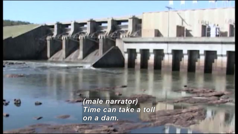 Dam with no water being released. Caption: (male narrator) Time can take a toll on a dam.