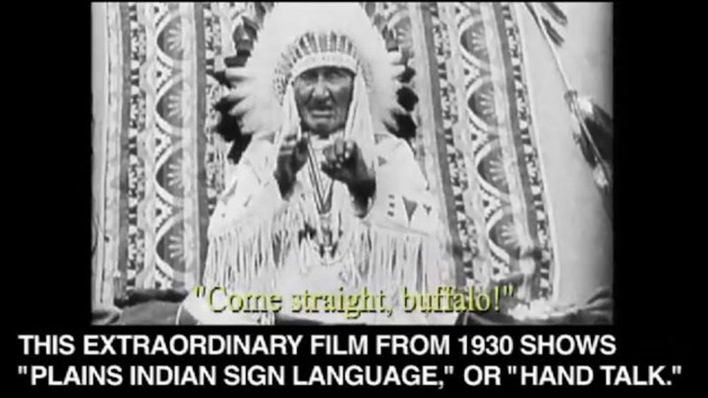 Native American man in a head dress and traditional clothing gesturing with his hands. Come straight, buffalo! Caption: This extraordinary film from 1930 shows "Plains indian sign language," or "Hand talk."