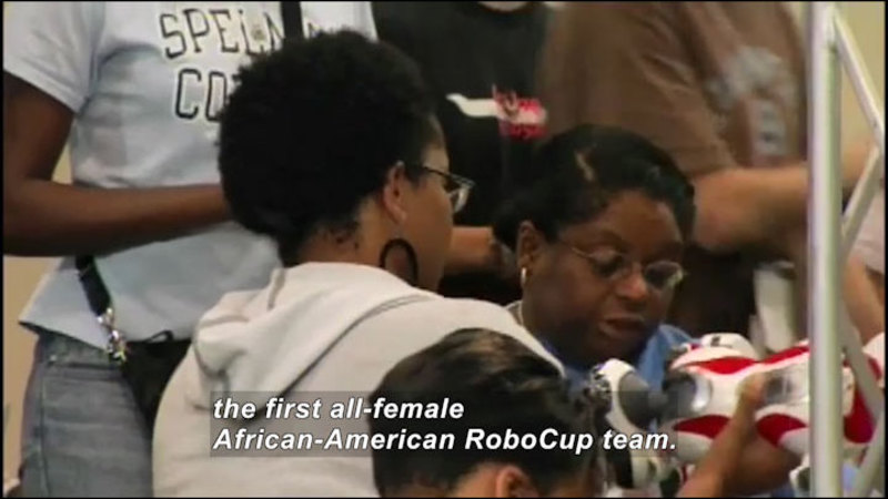 Several young people working on an object. Caption: the first all-female African-American RoboCup team.