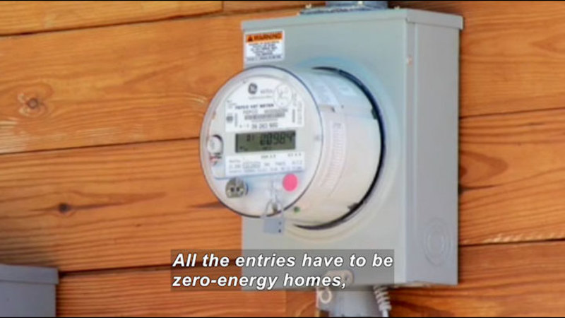 Electrical meter box attached to the outside of a building. Caption: All the entries have to be zero-energy homes,
