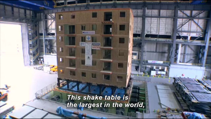 Platform in a warehouse holding a building suspended by struts. Caption: This shake table is the largest in the world,