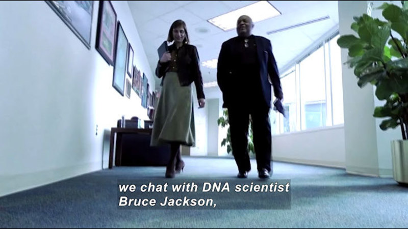 Two people walking down a hallway. Caption: we chat with DNA scientist Bruce Jackson,