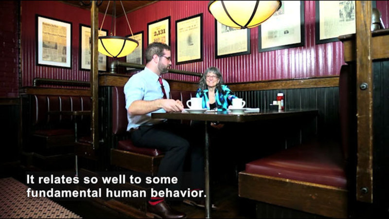 Two people sitting in a booth at a restaurant. Caption: It relates so well some fundamental human behavior.