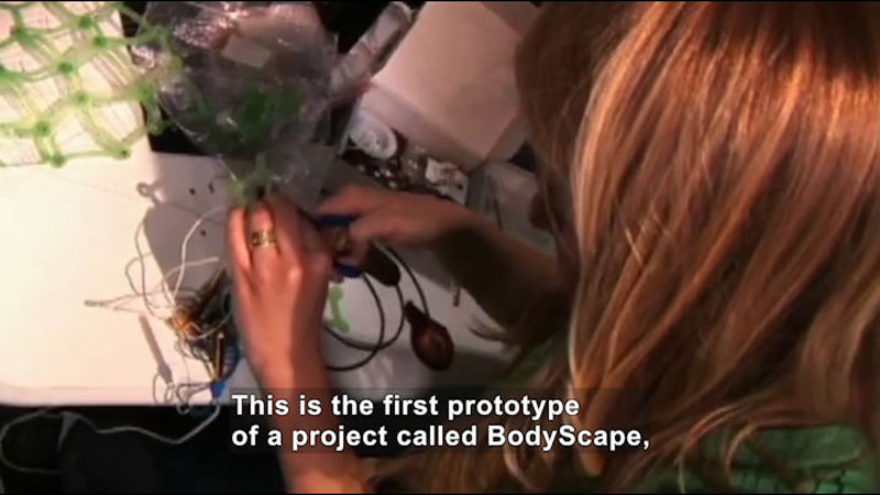 Person holding a tool and working on something with wires. Caption: This is the first prototype of a project called BodyScape,