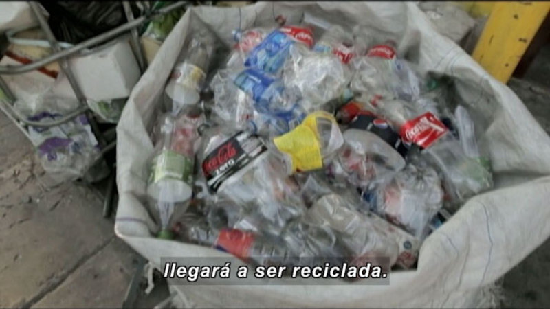 Large sack of crushed plastic soda bottles. Spanish captions.