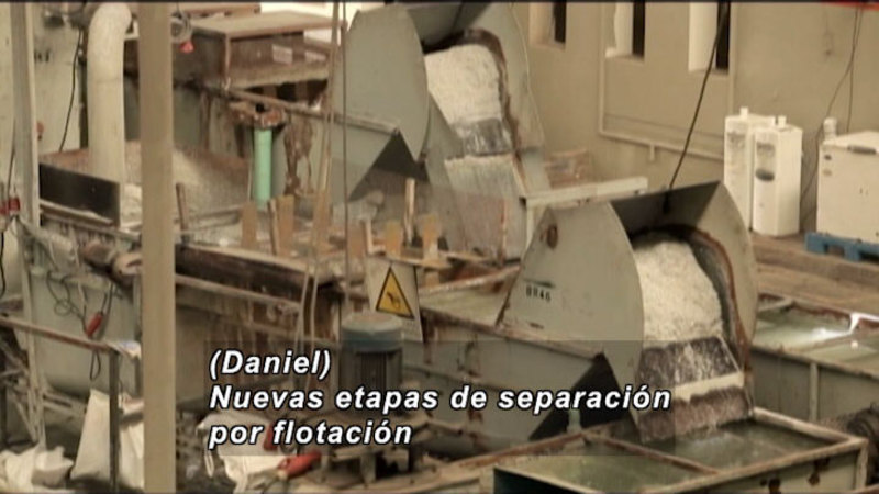 Industrial processing plant with conveyors dumping material into metal basins. Spanish captions.