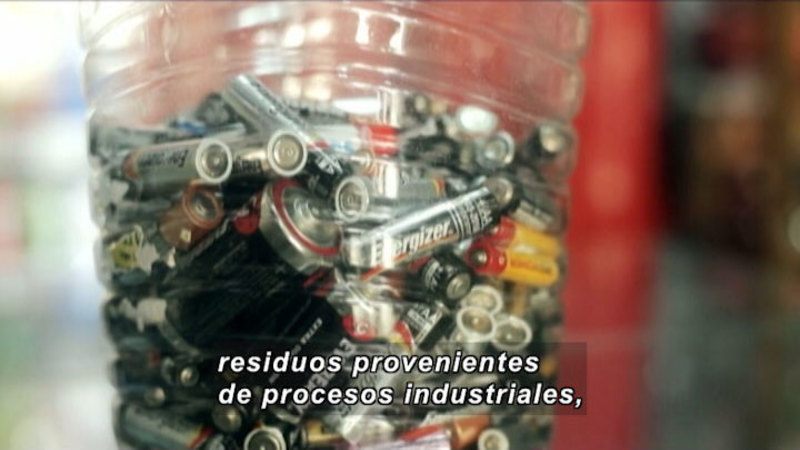 Different kinds of batteries held in a clear container. Spanish captions.