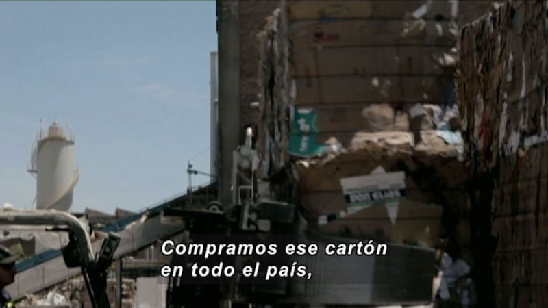 Giant stacks of compressed paper material being moved by industrial machinery. Spanish captions.