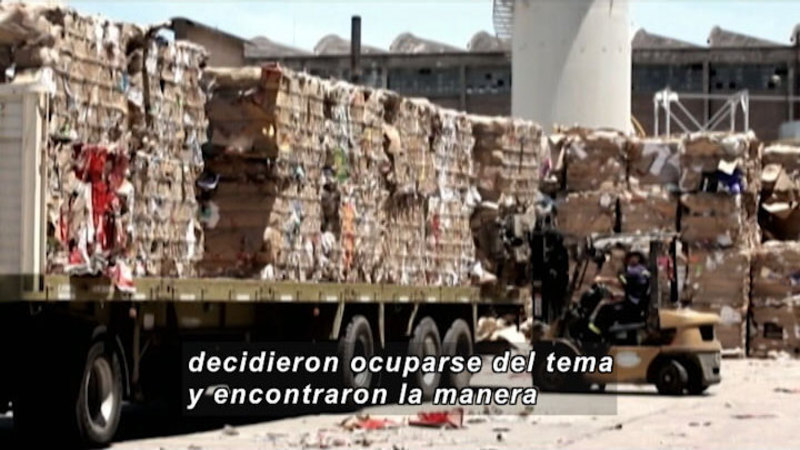 Forklift loading cubes of various materials onto a large flatbed truck. Spanish captions.