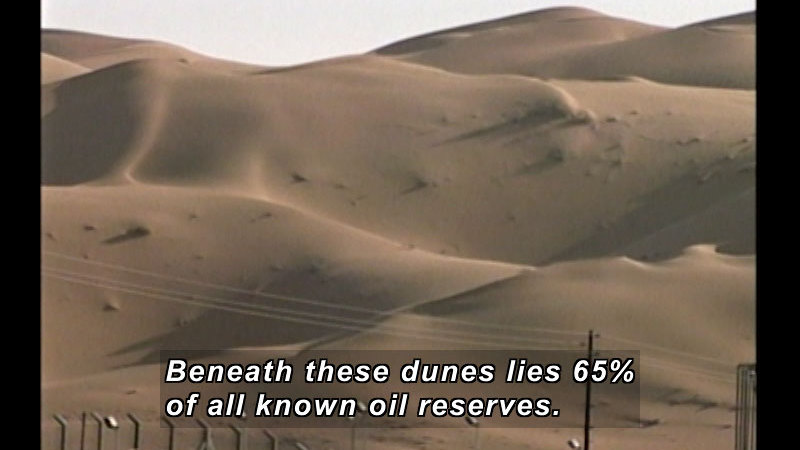 Rolling sand dunes with powerlines in the foreground. Caption: Beneath these dunes lies 65% of all known oil reserves.