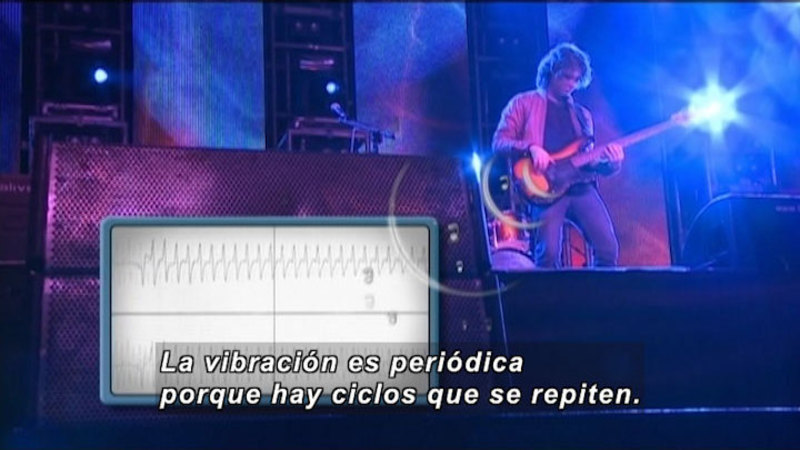 Person on stage playing a guitar with a machine measuring the vibration coming out of a speaker. Spanish captions.