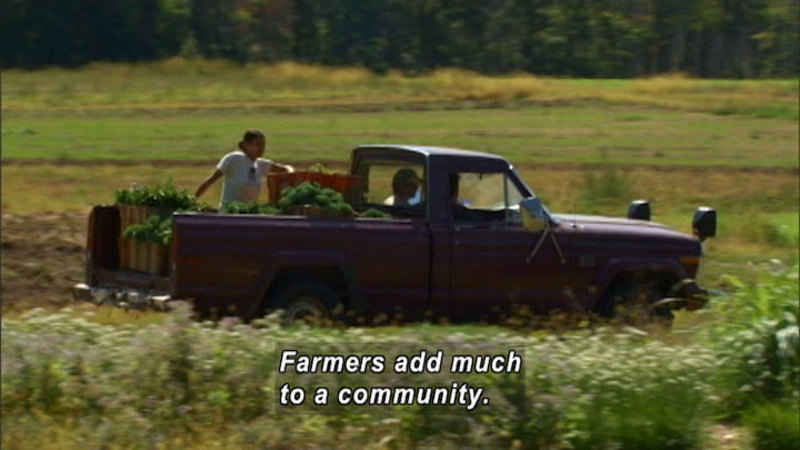 Pickup truck driving through a field, produce and a person riding in the back. Caption: Farmers add much to a community.