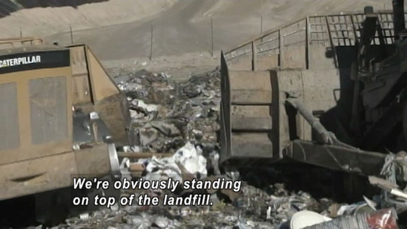 Large machinery on piles of garbage. Caption: We're obviously standing on top of the landfill.