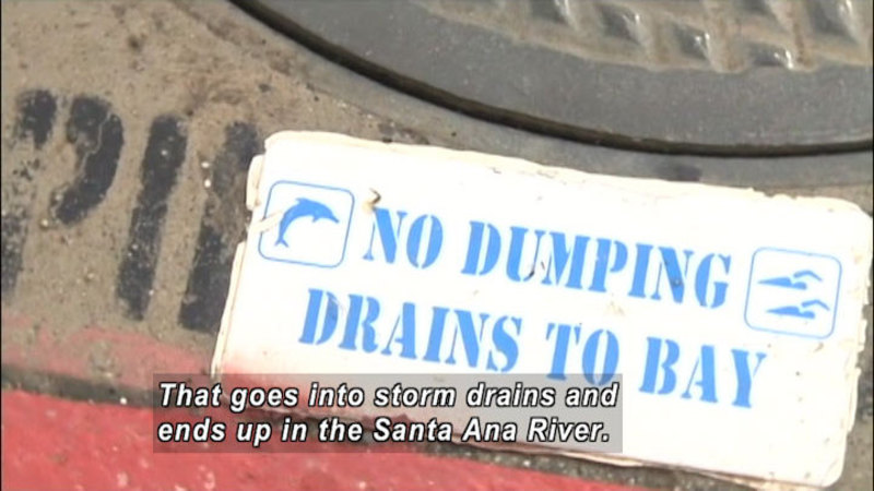 Edge of a manhole cover with "No Dumping Drains to Bay" printed on the ground. Caption: That goes into storm drains and ends up in the Santa Ana River.