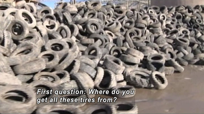 Long pile of thousands of old, dirty tires. Caption: First question: Where do you get all these tires from?
