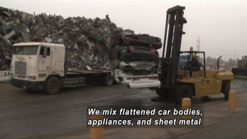 Industrial forklift moving several flattened cars. A giant pile of shredded metal in the background. Caption: We mix flattened car bodies, appliances, and sheet metal