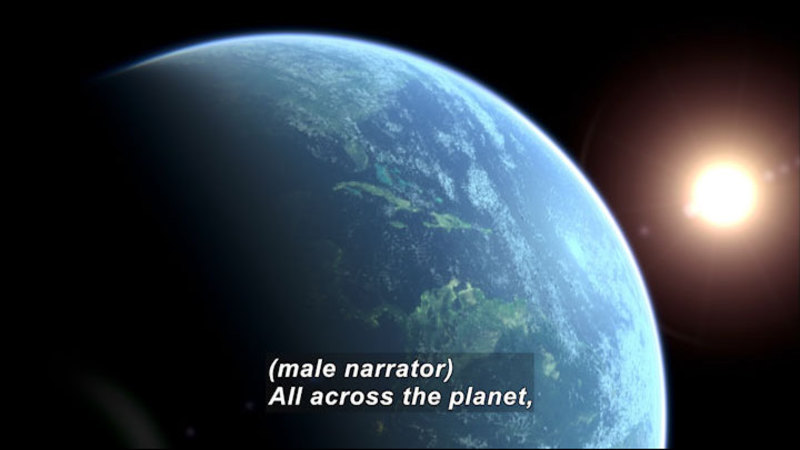 Earth as seen from space with the Sun visible behind it. Caption: (male narrator) All across the planet,