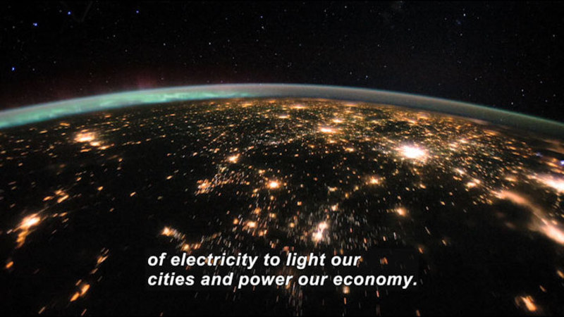 Earth at night as viewed from space. A network of glowing light is visible in unpopulated areas across the globe. Caption: of electricity to light our cities and power our economy.