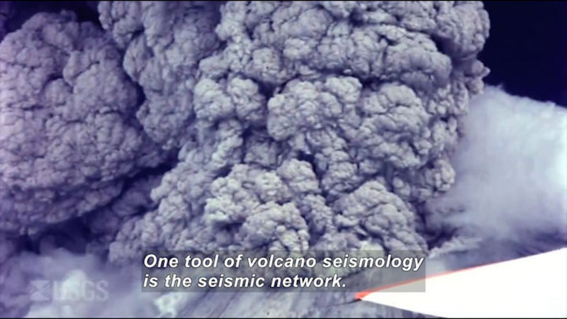Aerial view of billowing gray clouds of ash and smoke. Caption: One tool of volcano seismology is the seismic network.
