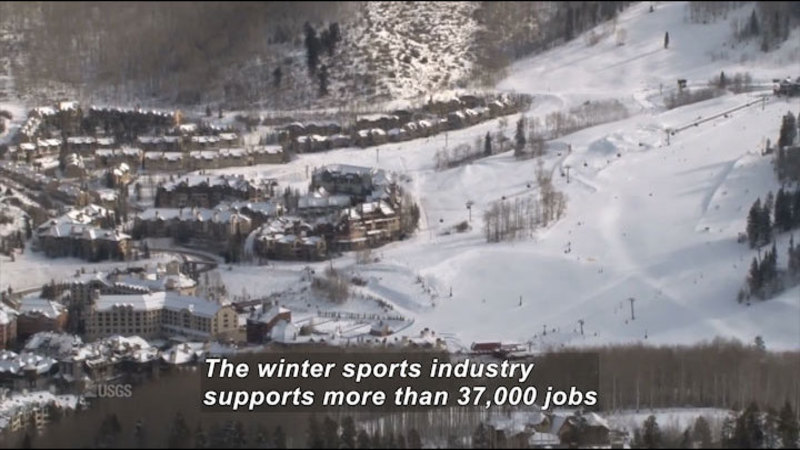 Multiple multistory snow covered building complexes at the foot of snow-covered slopes. Caption: The winter sports industry supports more than 37,000 jobs