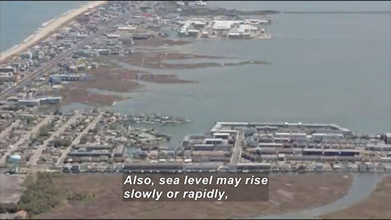 Ocean shoreline on one side and rising water on the other encircle a strip of densely populated buildings. Caption: Also, sea level may rise slowly or rapidly,