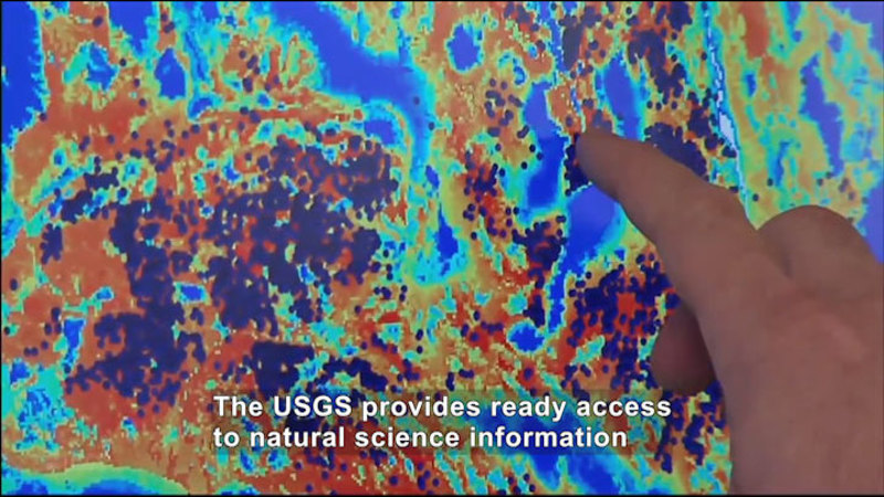 Person pointing to a spot on an image made of pixelated yellow to indigo spots. Caption: The USGS provides ready access to natural science information