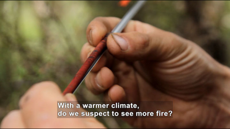 Closeup of hands holding a narrow, red tubular object. Caption: With a warmer climate, do we suspect to see more fire?