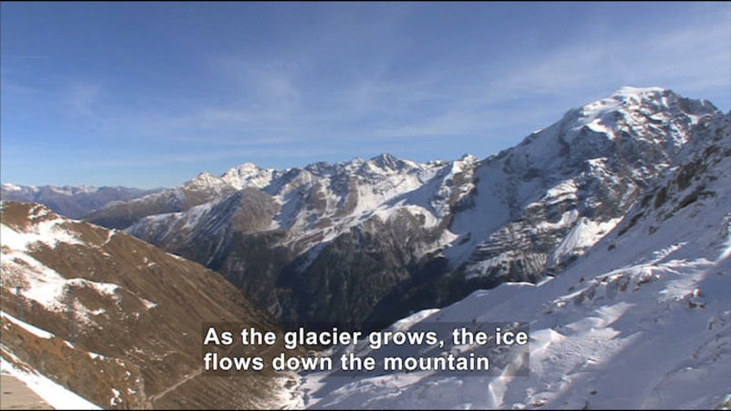 Steep rocky mountain partially covered in snow and ice. Caption: As the glacier grows, the ice flows down the mountain