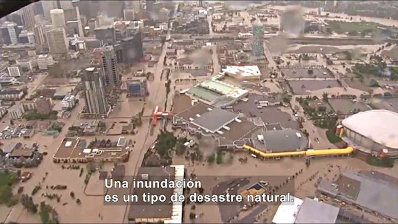 Aerial view of a city with muddy water filling the streets. Spanish captions.