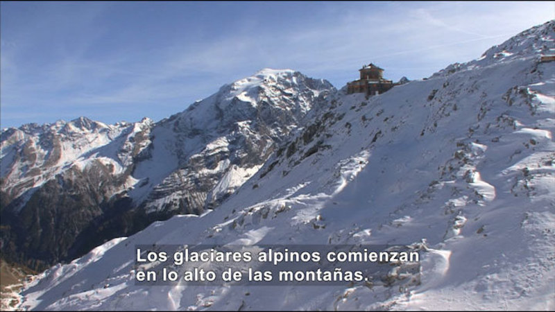 Steep rocky mountain partially covered in snow and ice. Spanish captions.