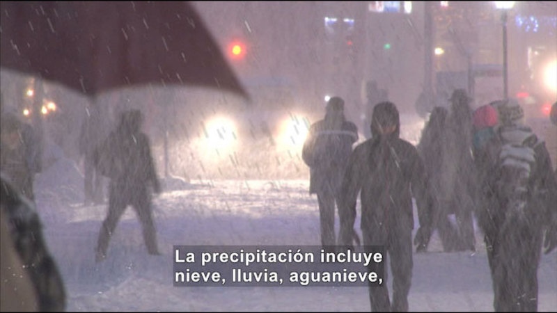People walking through a city while it's snowing. Spanish captions.