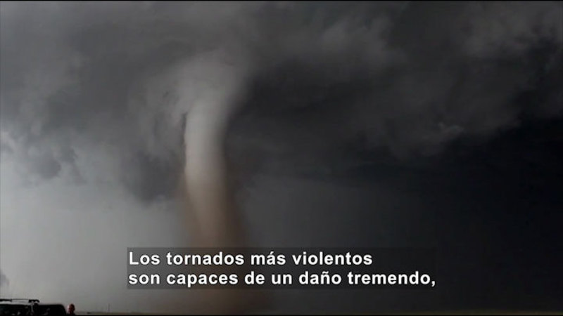 Funnel cloud descending from a cloud-covered sky. Spanish captions.