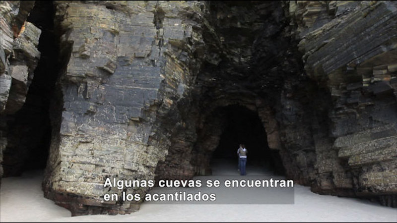 People standing in the mouth of a large cave. Spanish captions.