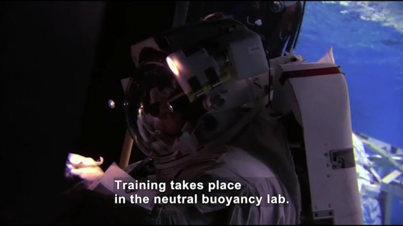 Astronaut in a space suit working on a machine. Caption: Training takes place in the neutral buoyancy lab.