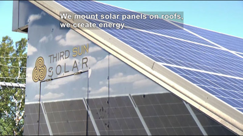 An angled roof covered in solar panels on top of a reflective building with "Third Sun Solar" and a logo on the side. Caption: We mount solar panels on roofs, we create energy,